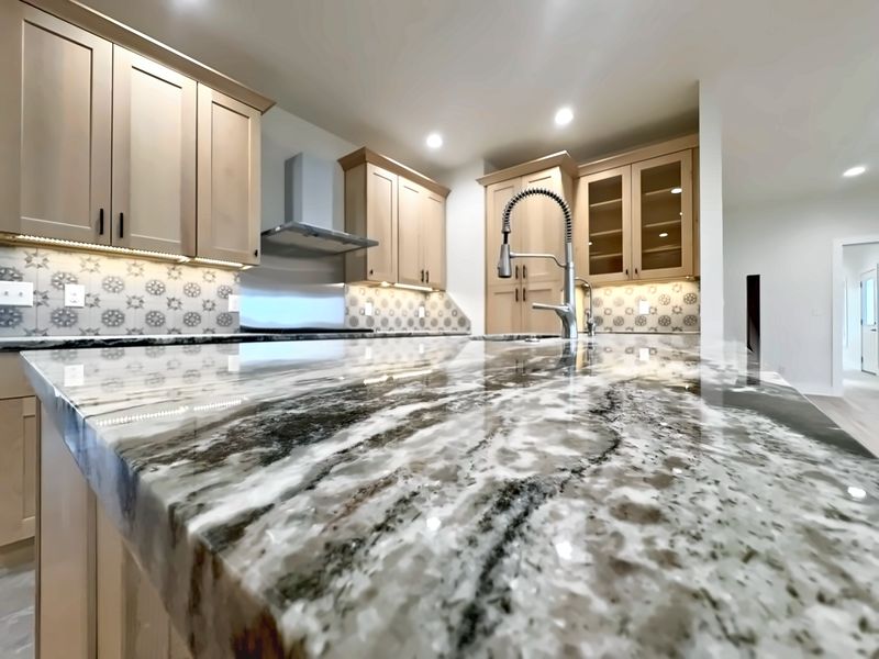 Polished granite kitchen island in front of maple shaker cabinets with a patterned tile backsplash