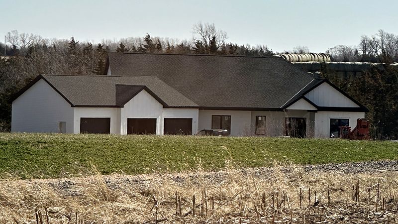 Finished white modern farmhouse-style ranch home with a three-stall attached garage, set in open farm country