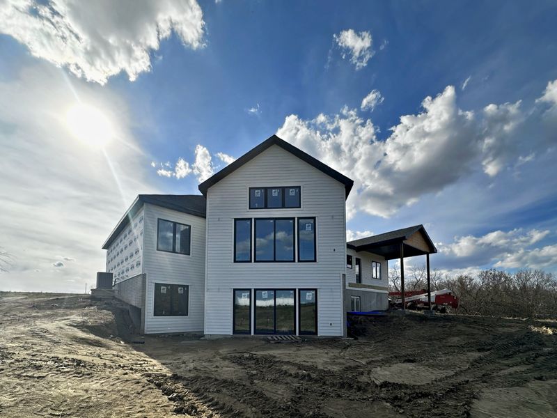 Rear of a white two-story modern farmhouse with tall black-framed windows and a covered patio