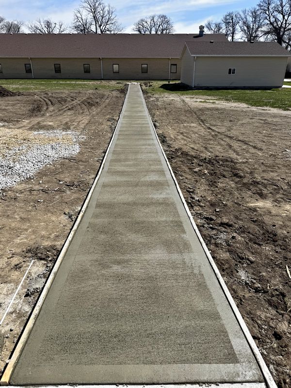 Freshly poured concrete sidewalk leading toward a building