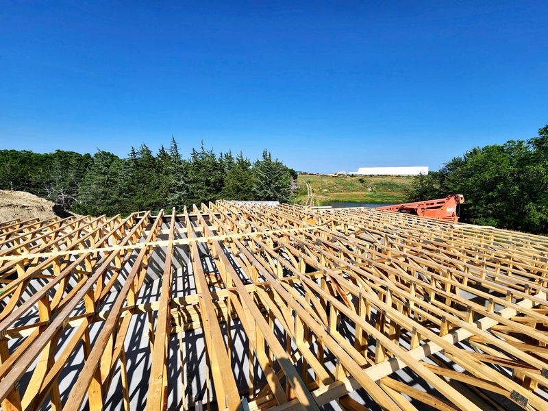 Roof trusses set on a new home with open field and pond views beyond
