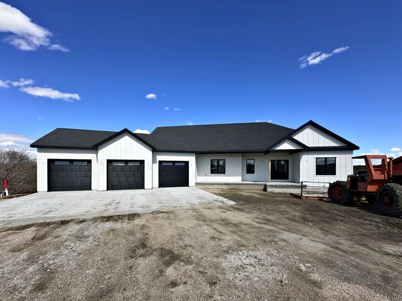 White board-and-batten ranch home with black trim and a three-car attached garage under a blue sky